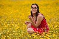 Girl with a red dress picking up flowers in a yellow field.