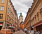 A narrow street in Stockholm with the clock tower of the Church of St. Nicholas (Sankt Nikolai kyrka) also known as Storkyrkan (The Great Church) and ...