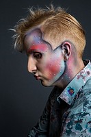 Portrait of beautiful young man with modern hairstyle, artistic multicolor makeup and rhinestones on the face. Studio shot. Black background.