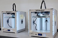 Two 3D three dimensional printers extruding Polylactic acid PLA polymer to print a plastic object.