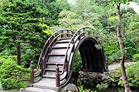 An unusual high arched pedestrian bridge over a stream in a landscaped Japanese Garden in California, USA.