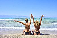 best friends, two vital girls sitting in bikini on beach and looking at sea. Dutch ethnicity. At holiday destination Chrissi Island, Crete, Greece