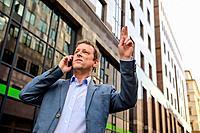 A middle age businessman standing and waving for a taxi while speaking on the phone.