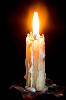 Lighted candle with the melted wax falling down in a chandelier isolated in black