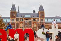 Tourists climbing on the I Amsterdam giant letters marketing slogan with Rijksmuseum behind, Museumplein (Museum Square), Amsterdam, Holland.