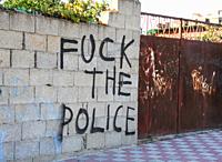 Graffiti in a breeze block wall against the police with rusty gates in Cagliari, Sardinia, Italy