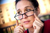 A casual portrait of a pretty 39 year old brunette woman with glasses looking away from the camera with an expression of concern.