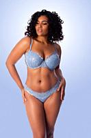 Beautiful happy plus size sexy woman with curly hair in light blue lingerie bra and thong underwear.