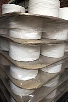 Confrontational flat industrial spools of white thread packaged with layers of thick corrugated card dividers and shrink wrapped in reflective polythe...