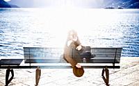 Woman Sitting on a Bench on the Waterfront and Looking Back with Sun Reflection in Ascona, Switzerland.