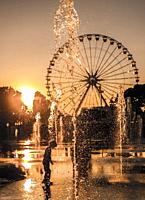 Child Playing in the Water Fountain with Ferris Wheel in Background in Sunset in Nice, France.