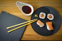 Sushi on a wooden table on black slate plate with soy sauce and chopsticks.