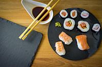 Sushi on a wooden table on black slate plate with soy sauce and chopsticks.