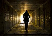 Female figure walking toward the light at the end of the tunnel