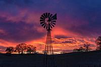 Sunset storm clouds and colors form a backdrop for a foothill farm´s windmill. Sierra Nevada Foothills, California, USA
