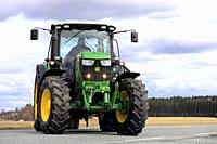 Farmer makes a right turn with John Deere 6150R tractor and agricultural trailer off main road. Jokioinen, Finland - April 30, 2018.