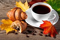 Cup of black coffee with croissants. Grains of coffee and autumn maple leaves on a wooden table.