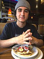 Young Man sitting in restaurant eating pancakes