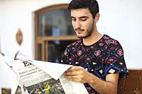 Young man reads newspaper at outdoor cafe, Salobreña, Spain.
