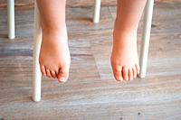 Feet of a child sitting in a chair. Natural lighting.