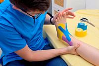 Physiotherapist applying kinesiology tapes on injury leg.