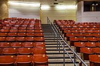 Row of empty chairs, with stairs in the middle, in an auditorium.