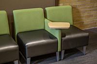 Two identical chairs, with a desk between them, in a college lobby.