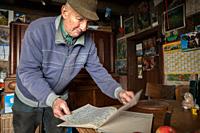 Friendly elderly man in his kitchen showing his hand-written book with notes about the weather and important incidents. Germany.