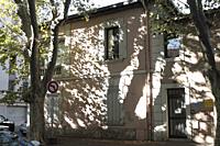 Plane trees cast dramatic shadows and reflections on a traditional pink and white shuttered house behind a residents only road sign in Avignon, Vauclu...