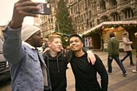 young men taking selfie in front of Neues Rathaus and Christmas market at Marienplatz in Munich, Germany.