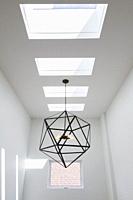 Skylight windows and black steel hexagonal lighting fixture with five clear glass bulbs hung above the staircase inside a modern cube style home