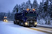 Salo, Finland - January 25, 2019: Two trucks, Scania V8 for limestone haul in the front at speed with beautiful lights lighting up the dark rural road...