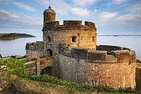 St Mawes Castle on Cornwall's Roseland Peninsula illuminated by late evening sunlight in late June with the lighthouse on St Anthony Head in the dista...
