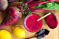 Red beet juice in a glass on a wooden table with whole beets and lemons, top view.