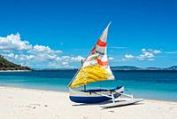 Malagasy outrigger pirogue with colorful makeshift sails on the white beach.