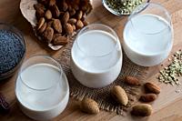 Three glasses of vegan plant milk - almond milk, poppy seed milk and hemp seed milk, with shelled and unshelled almonds, poppy seeds and hemp seeds on...