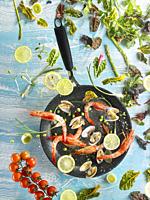 Composition with vegetables and seafood, flying over a frying pan, with blue background.