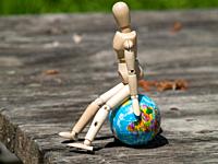 A wooden mannequin sitting on a world ball. Concept of ecology, globalization.