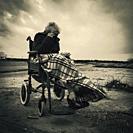 Old woman in wheelchair shielding herself from the wind