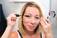 Beautiful blonde woman applying mascara on her eyelashes.