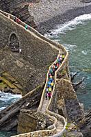 Visitors crossing teh stone bridge to the islet Gaztelugatxe near Bakio, Costa Vasca, Bay of Biscay, Basque Country, Spanien.