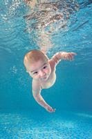 Little baby boy learning to swim underwater in a swimming pool. Healthy family lifestyle and children water sports activity. Child development, diseas...