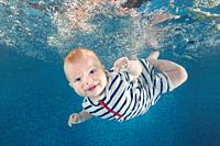Little baby boy in a striped suit learns to swims underwater in the swimming pool. Healthy family lifestyle and children water sports activity. Child ...