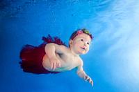 Funny face portrait of baby girl in a red skirt swimming and diving underwater with fun in the pool. Healthy family lifestyle and children water sport...