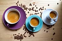 White porcelain cups, cyan and magenta with expresso coffee, on wooden board decorated with roasted coffee beans