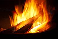 Approaching logs burning between the flames to fan the fire that illuminates a black night.