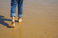 Man´ s legs walking along wet sand.