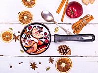 mulled wine with spices and fruits in an aluminum container on a white wooden background, top view.  