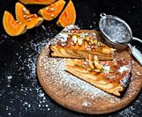 pieces of pumpkin pie on a round wooden board are sprinkled with sugar powder, a black wooden background with pieces of fresh pumpkin.  