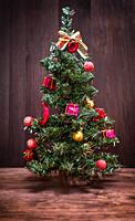 Artificial Christmas tree with toys on a brown wooden background.  